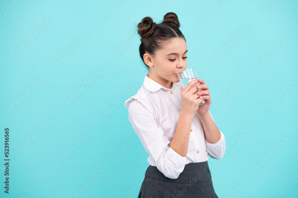 Teenage girl drinking water from glass on blue background. Daily life health. Drink water for health care and body balance. Thirsty child, dehydration. Teenage girl drinking water from glass on blue background. Daily life health. Drink water for health care and body balance. Thirsty child, dehydration.