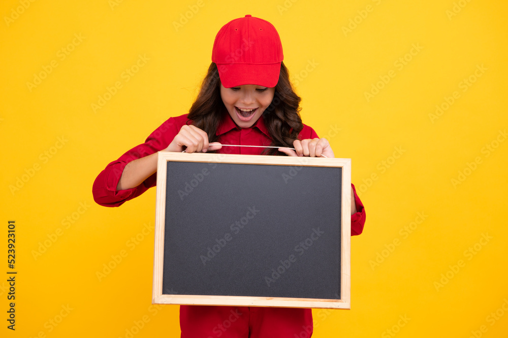 Excited child girl in red uniform and cap hold blackboard. Teenage girl hold blackboard isolated on yellow background. Copy space on empty board, mock up. Excited teenager girl. Excited child girl in red uniform and cap hold blackboard. Teenage girl hold blackboard isolated on yellow background. Copy space on empty board, mock up. Excited teenager girl.