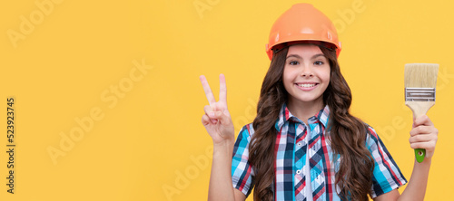 Renovation child, happy teen girl in construction helmet hold painting brush show peace gesture, decoration. Child builder in helmet horizontal poster design. Banner header, copy space.