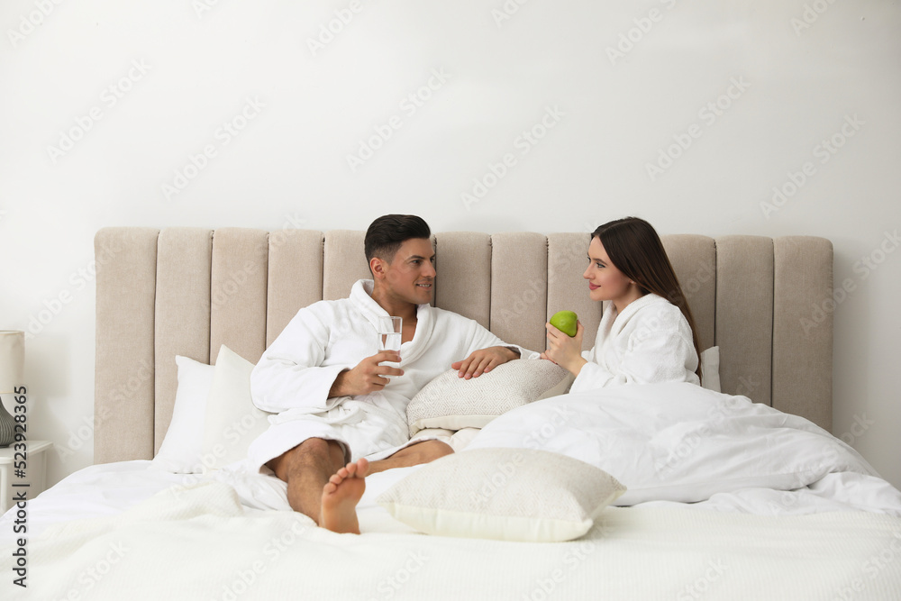 Fototapeta premium Happy couple in bathrobes resting on bed at home