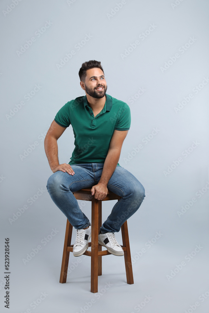 Handsome young man sitting on stool against light grey background Handsome young man sitting on stool against light grey background
