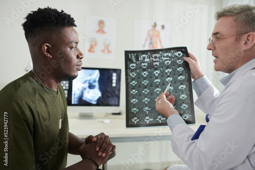 Serious doctor pointing at MRI image of spine when talking to military man suffering from back pain