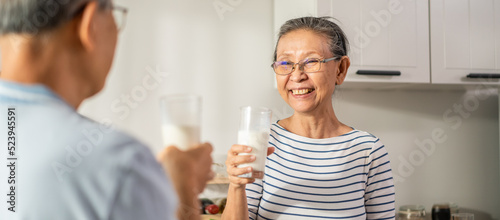 Asian senior elderly couple drink a glass of milk in kitchen at home. 