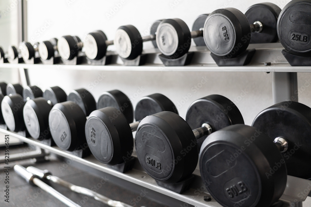 Stand with dumbbells. Sports and fitness room. Weight Training Equipment. Black dumbbell set, many dumbbells on rack in sport fitness center Stand with dumbbells. Sports and fitness room. Weight Training Equipment. Black dumbbell set, many dumbbells on rack in sport fitness center