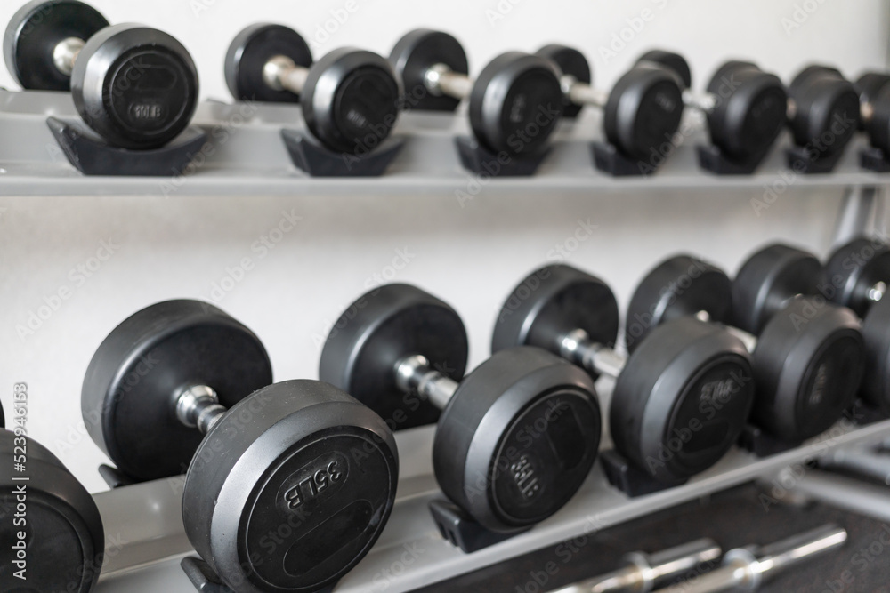 Stand with dumbbells. Sports and fitness room. Weight Training Equipment. Black dumbbell set, many dumbbells on rack in sport fitness center Stand with dumbbells. Sports and fitness room. Weight Training Equipment. Black dumbbell set, many dumbbells on rack in sport fitness center
