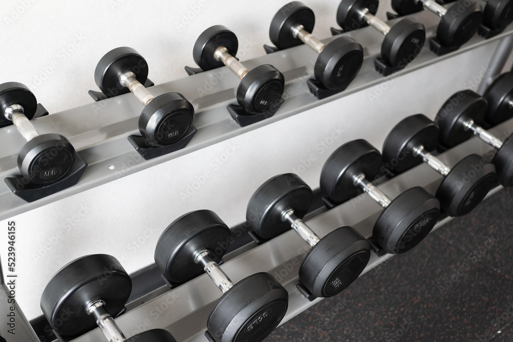 Stand with dumbbells. Sports and fitness room. Weight Training Equipment. Black dumbbell set, many dumbbells on rack in sport fitness center Stand with dumbbells. Sports and fitness room. Weight Training Equipment. Black dumbbell set, many dumbbells on rack in sport fitness center