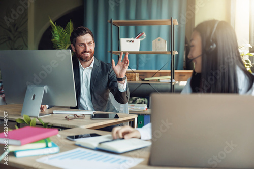 Male office worker waving hi to colleague sitting at neighboring table