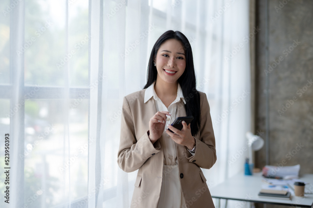 Beautiful Asian businesswoman is using her smartphone to chat with customers in a relaxed workplace with a smile and a good mood. Beautiful Asian businesswoman is using her smartphone to chat with customers in a relaxed workplace with a smile and a good mood.