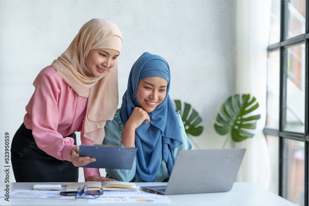 Fototapeta premium Two beautiful Muslim Asian businesswomen wearing hijab We are discussing work in various field there is an exchange of idea. and exchanging knowledge by using a laptop computer to work.