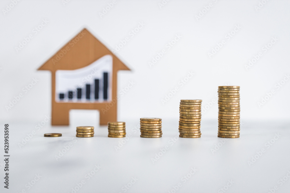interest rates for loans and real estate prices going up, graph with upward trend with growing stacks of coins in front of cardboard house interest rates for loans and real estate prices going up, graph with upward trend with growing stacks of coins in front of cardboard house
