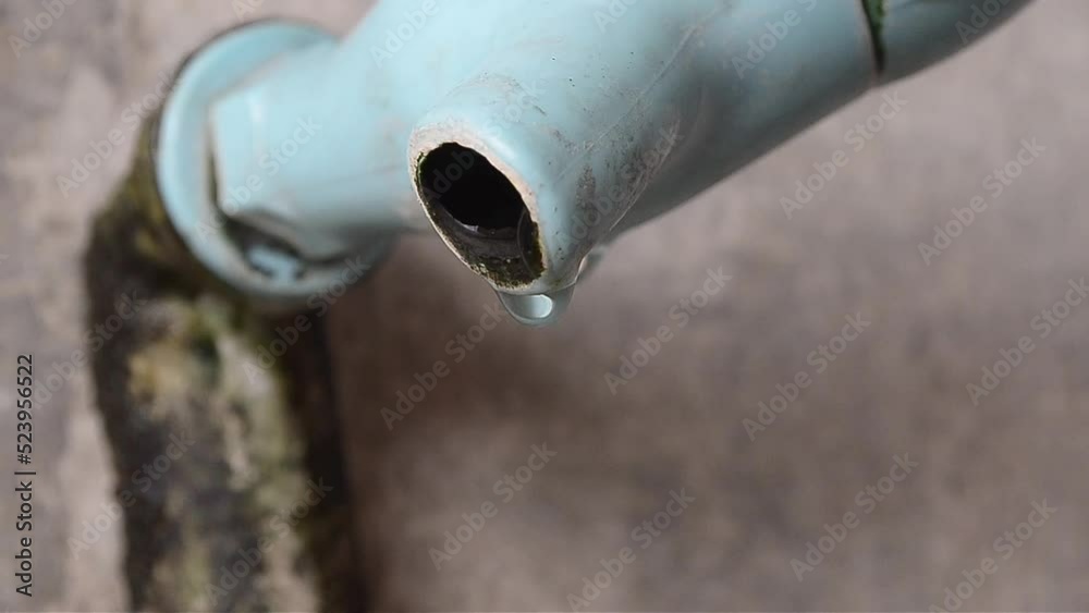 clear water dripping slowly from the blue plastic faucet. clear water flow from old broken pipes and mossy against the background of shabby building walls. water dripping from the faucet. clear water dripping slowly from the blue plastic faucet. clear water flow from old broken pipes and mossy against the background of shabby building walls. water dripping from the faucet.