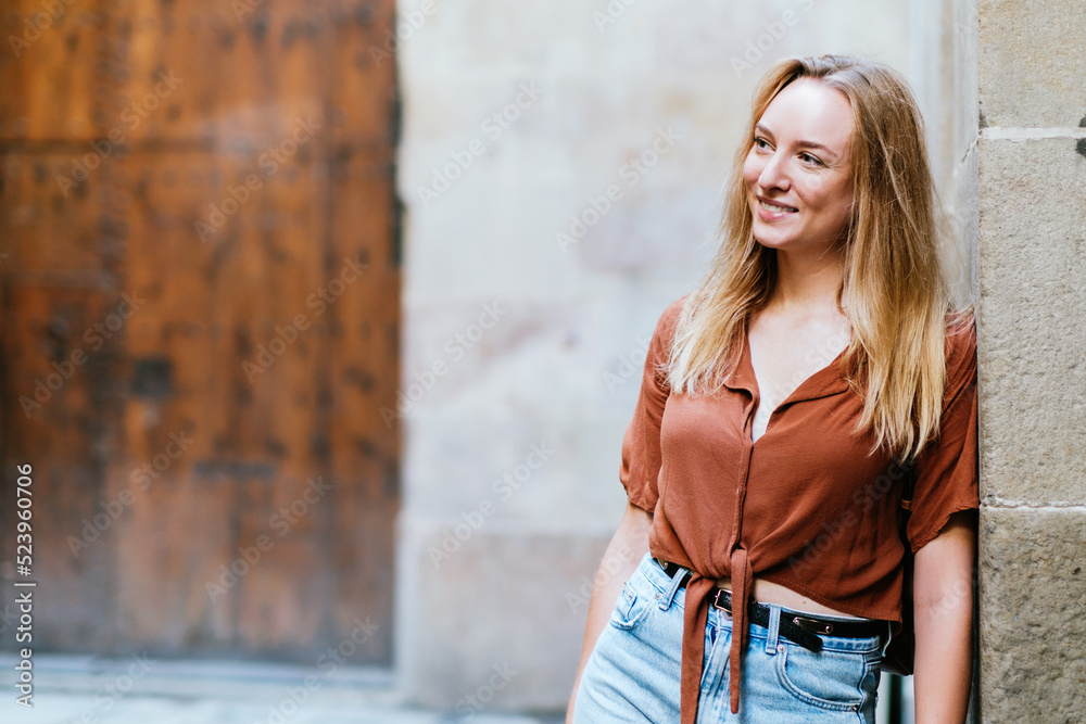 blonde caucasian female tourist leaning on a wall of Barcelona old town. She is smiling and looking to one side