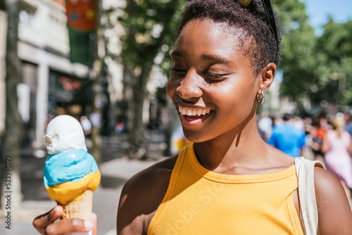 cheerful african american woman smiling while looking to her ice-cream on a summer day