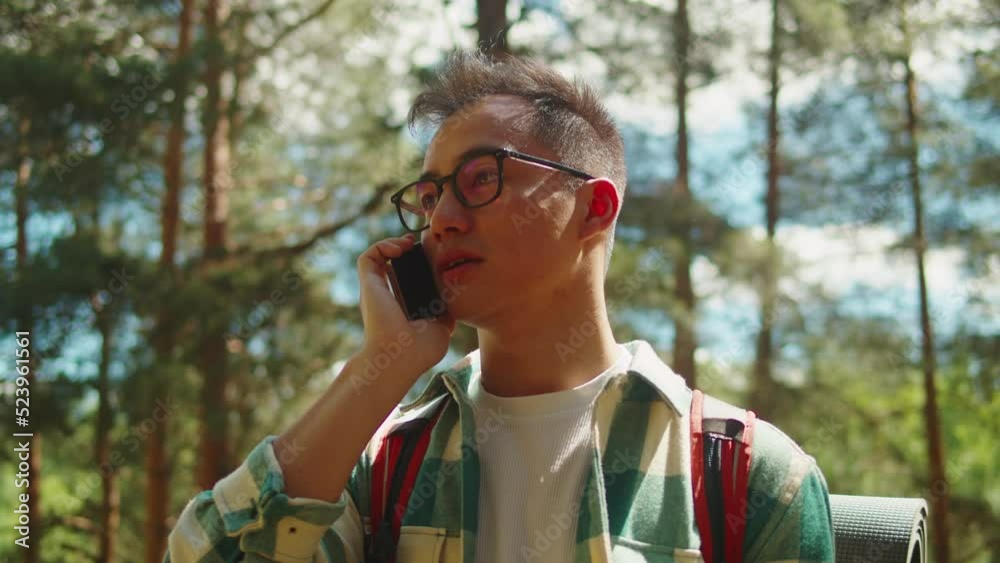 Asian man tourist calling on smartphone. Young hiker walking in forest camp, using mobile phone, traveling and hiking alone. Summer tourism, wild nature. 