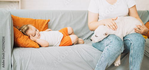A girl sitting on a sofa strokes a puppy on her lap next to a little girl.