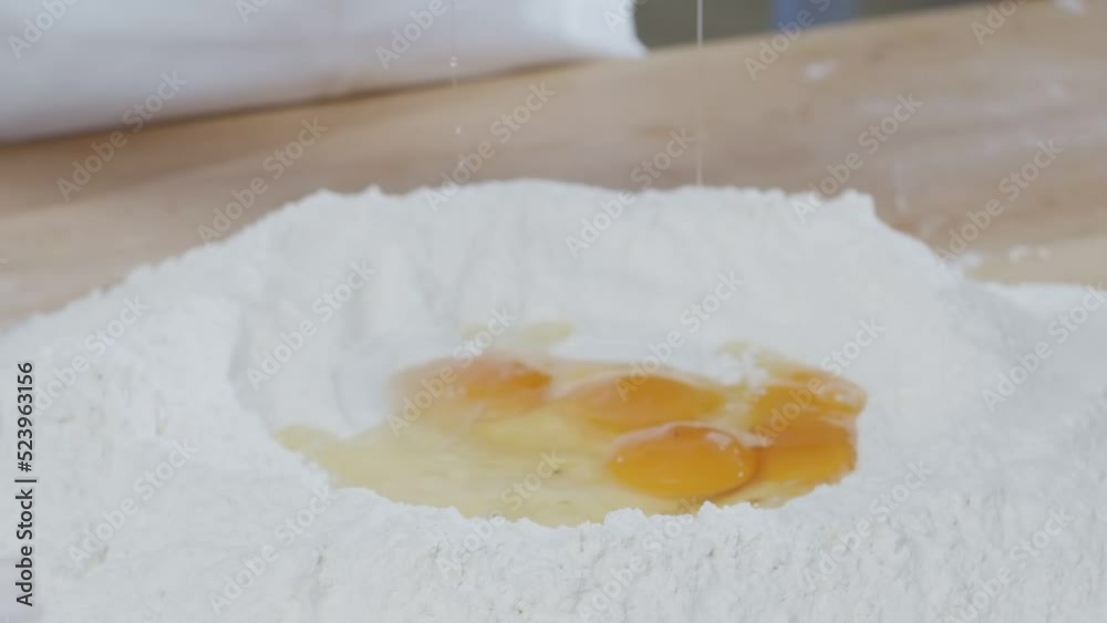 Baker break eggs to the flour lying on the wooden cooking table Baker break eggs to the flour lying on the wooden cooking table