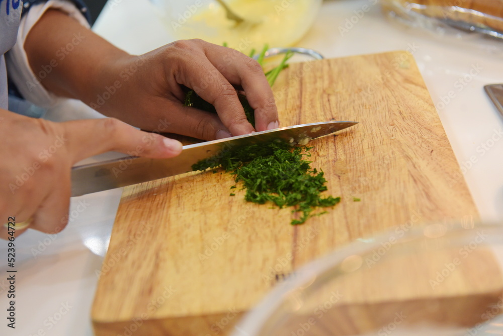 Almaty, Kazakhstan - 08.28.2015 : Slicing greens on a wooden board in the kitchen. Almaty, Kazakhstan - 08.28.2015 : Slicing greens on a wooden board in the kitchen.