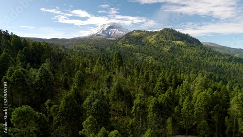 backwards drone shot showing the snowy top of the popocatepetl volcano in mexico city and the lush forests that surround it photo