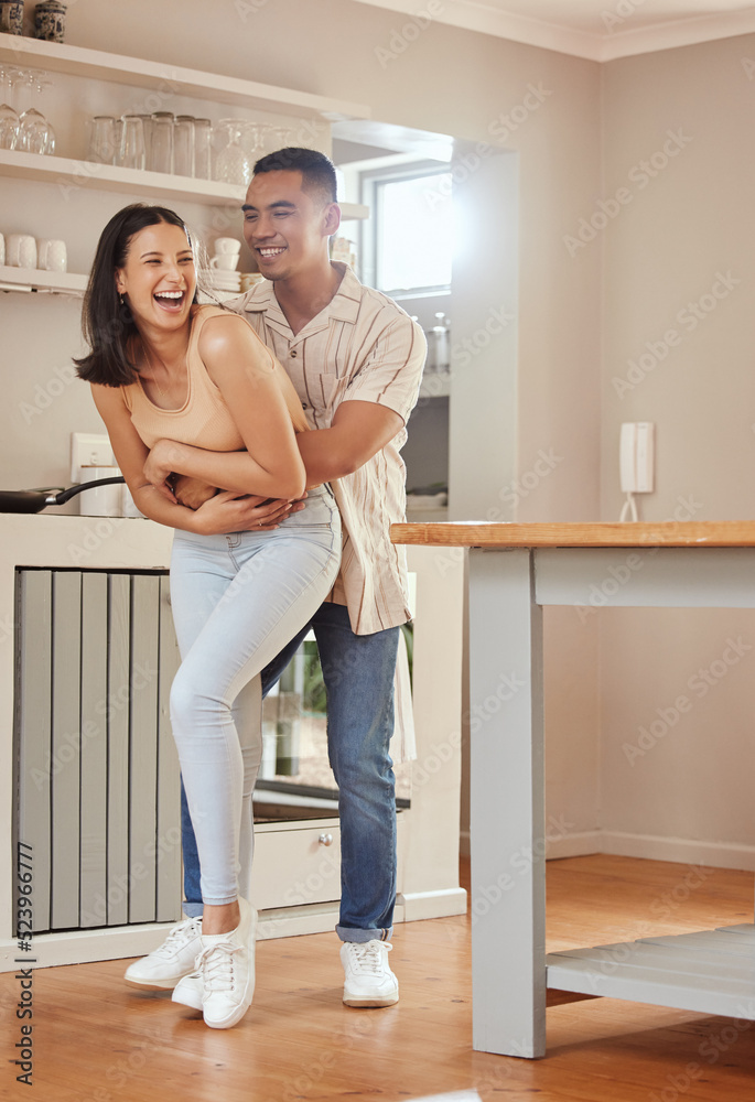 Interracial, fun and carefree couple hugging, bonding and laughing while relaxing together at home. Caring, loving and relaxed boyfriend and girlfriend enjoying romantic holiday and embracing