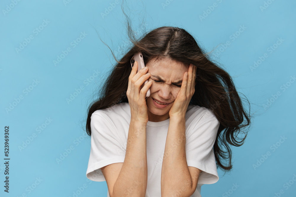a close portrait of a sad, depressed woman with her hair blowing in the wind during a telephone conversation. Horizontal photo on a light blue background a close portrait of a sad, depressed woman with her hair blowing in the wind during a telephone conversation. Horizontal photo on a light blue background