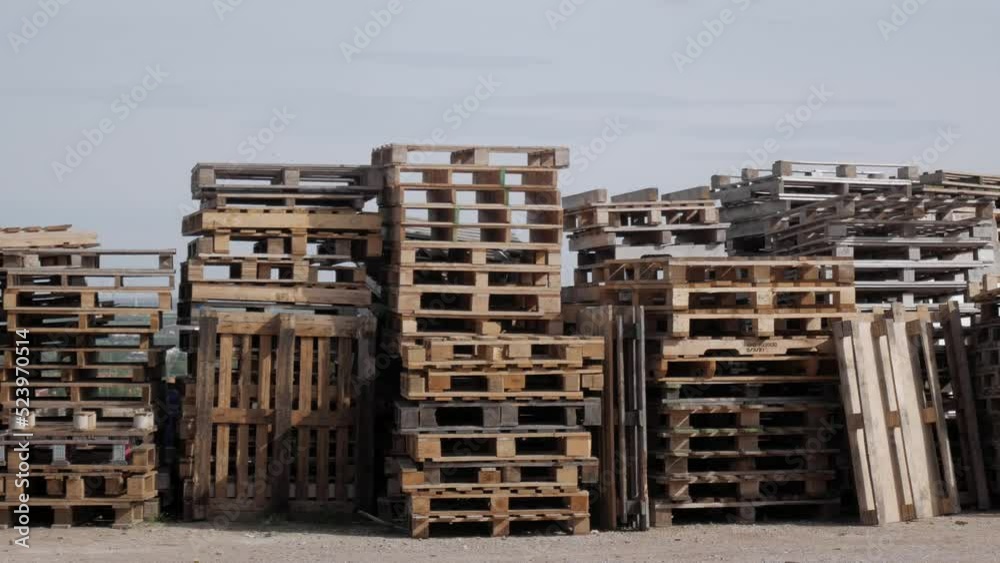Panning shot of columns of pallets piled vertically outdoors. Different colours and sizes. Some organized others not. Horizon behind. Mountains on skyline. Panning shot of columns of pallets piled vertically outdoors. Different colours and sizes. Some organized others not. Horizon behind. Mountains on skyline.