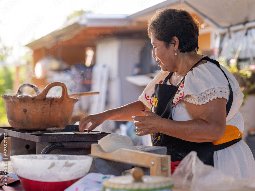 Indigenous woman making tortillas by hand and cooking them on the