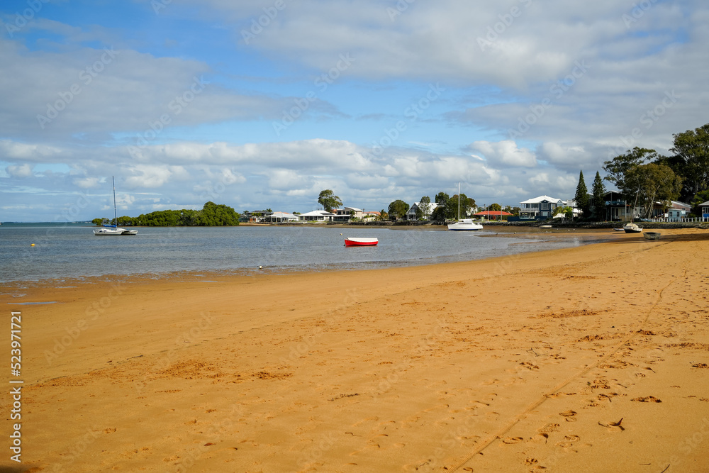 Obraz premium Sandy beach with boats, houses in the background and pretty cloudy sky. Victoria Point, Queensland, Australia 