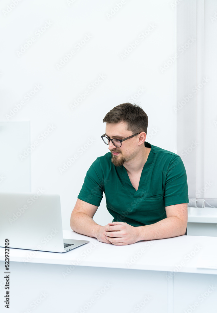 Professional young physician sitting with computer. Handsome medical specialist working with laptop. Professional young physician sitting with computer. Handsome medical specialist working with laptop.