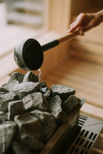 Fotografie Hand of young woman pouring water on hot rocks in the sauna
