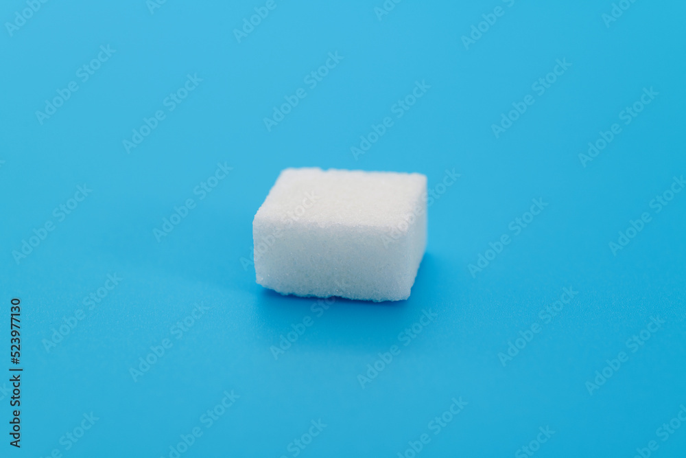 One sugar cube on blue background One sugar cube on blue background