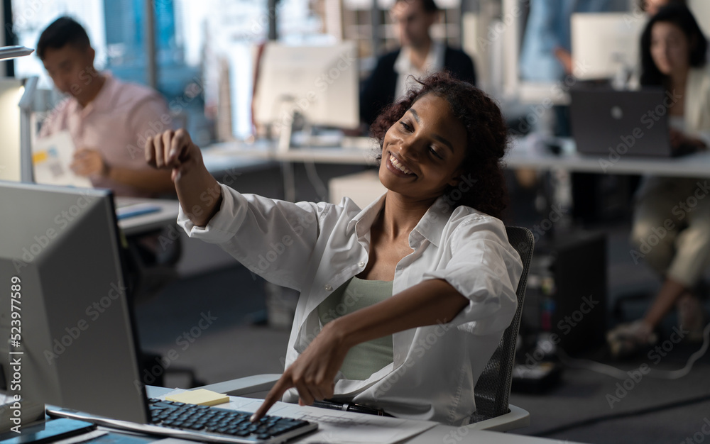 Bored African American female employee silly typing on a keyboard at her working desk in a large busy office, other workers in the background Bored African American female employee silly typing on a keyboard at her working desk in a large busy office, other workers in the background