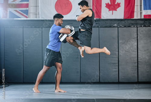 Healthy professional coach sparring and training male kickboxer indoors. Practice sports, exercise and fitness. Two muscular men fighting, jumping and blocking kicks with discipline in class.