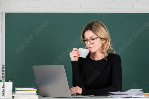 Portrait of teacher or female tutor working at table and drinking coffee in college or high school. Young women student studying in class.