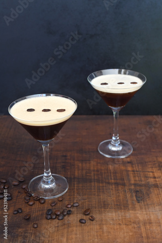 Glasses of espresso martini with coffee beans on wooden table and black background