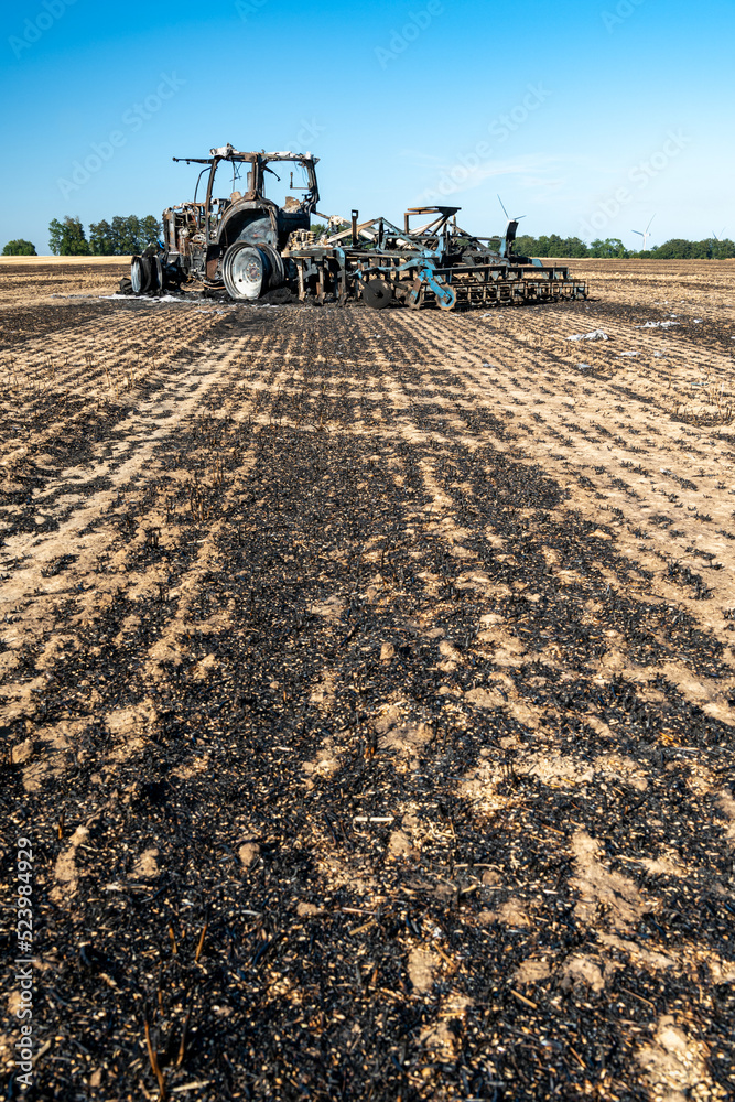 Fototapeta premium Feux de champs, carcasse de tracteur et d'un déchaumeur calciné suite à un incendie de chaumes lors de forte canicule