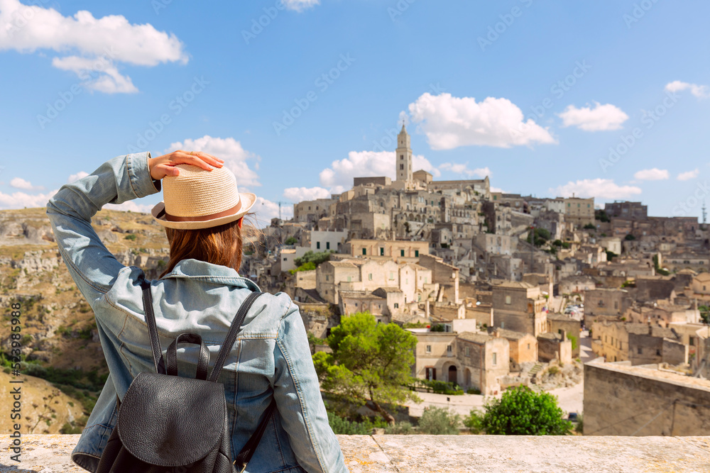 tourist girl with hat  looking the stunning view of the Sassi di Matera in Italy on a warm summer day. Travel destination, adventure, success and exploration concept.