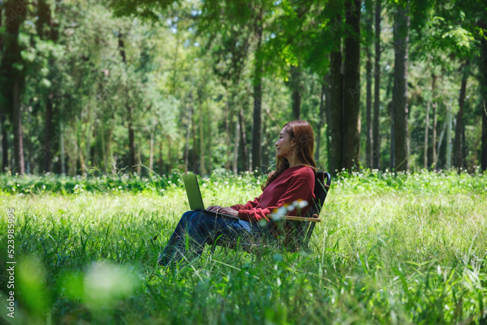 A beautiful asian woman working and typing on laptop keyboard while sitting on a chair in the park