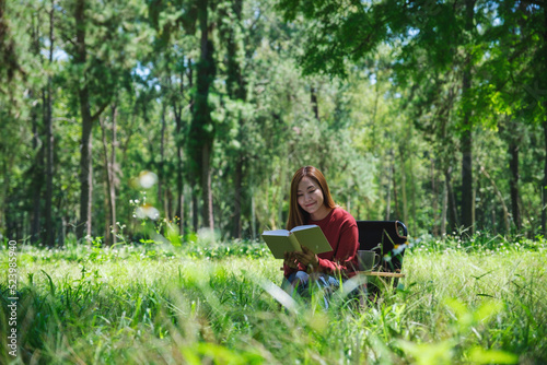 Portrait of a beautiful young asian woman reading a book while sitting on a camping chair in the park