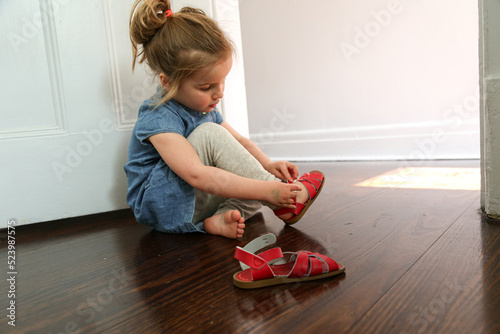 close up shot of a girl wearing blue blouse and grey pants sitting on the floor putting on sandals