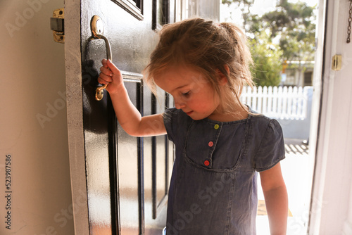 close up shot of a smiling girl wearing blue dress holding the door handle while looking down photo
