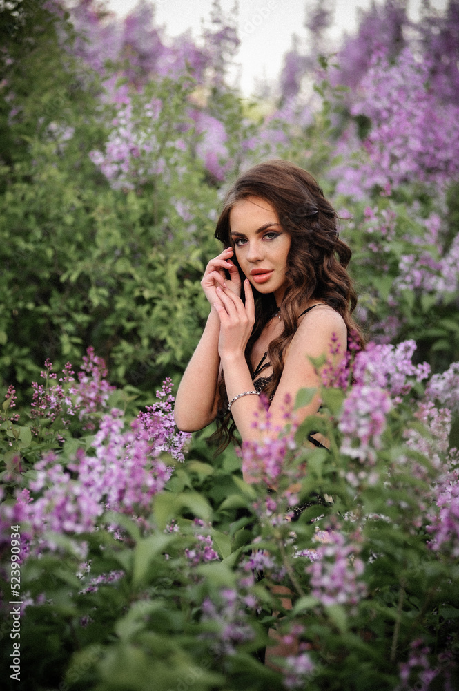 a beautiful girl with makeup and hair styling in underwear stands in a garden with lilacs on a summer evening a beautiful girl with makeup and hair styling in underwear stands in a garden with lilacs on a summer evening
