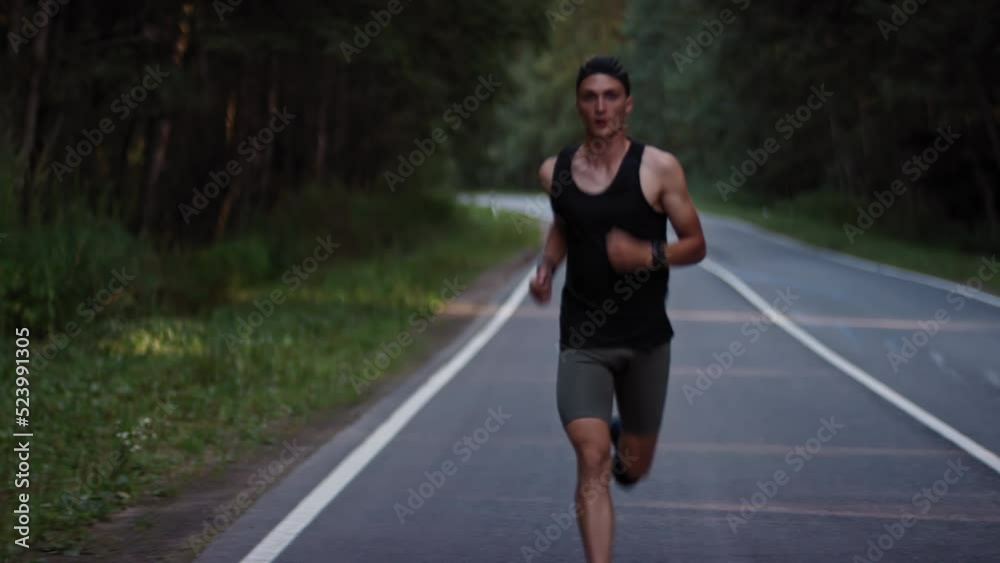 A professional athlete in a sports uniform runs along an asphalt road track in the forest on a summer day A professional athlete in a sports uniform runs along an asphalt road track in the forest on a summer day