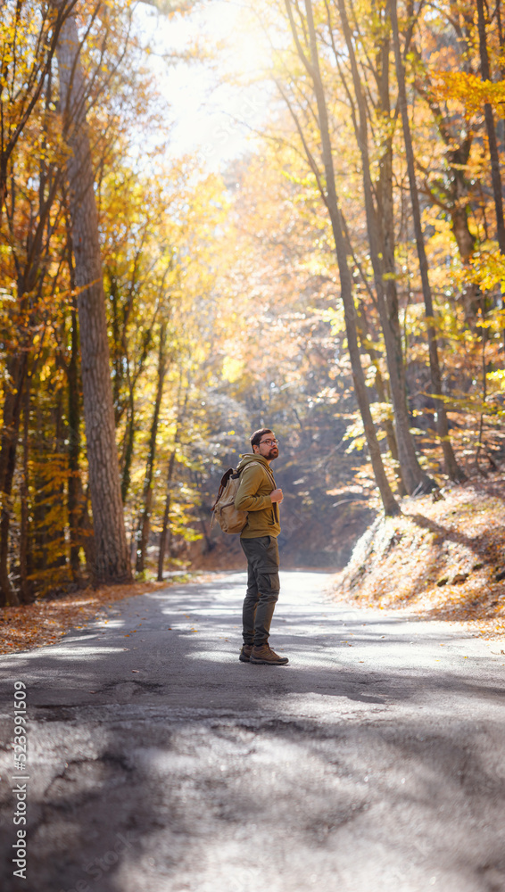 Young handsome man posing in autumn forest. young hipster guy with backpack , traveller standing in woods, Hiking, Forest, Journey, active healthy lifestyle, adventure, vacation concept.
