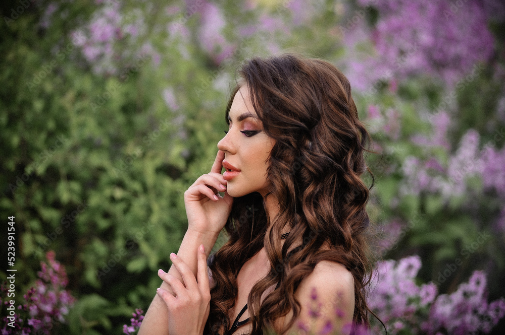 a beautiful girl with makeup and hair styling in underwear stands in a garden with lilacs on a summer evening a beautiful girl with makeup and hair styling in underwear stands in a garden with lilacs on a summer evening