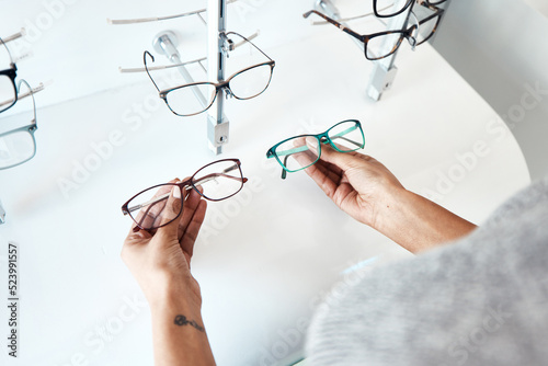Fototapeta Naklejka Na Ścianę i Meble -  Buying, looking and shopping for glasses at a retail eyewear store and optometrist inside. Customer holding shop stock trying to decide on a new modern style, trendy and stylish frames to buy on sale