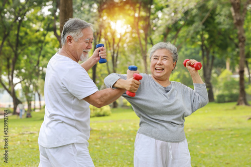 Happy and smiling asian senior couple doing arm work out and lifting dumbbell exercise with relaxation for healthy in park outdoor after retirement. Health care elderly outdoor lifestyle concept.