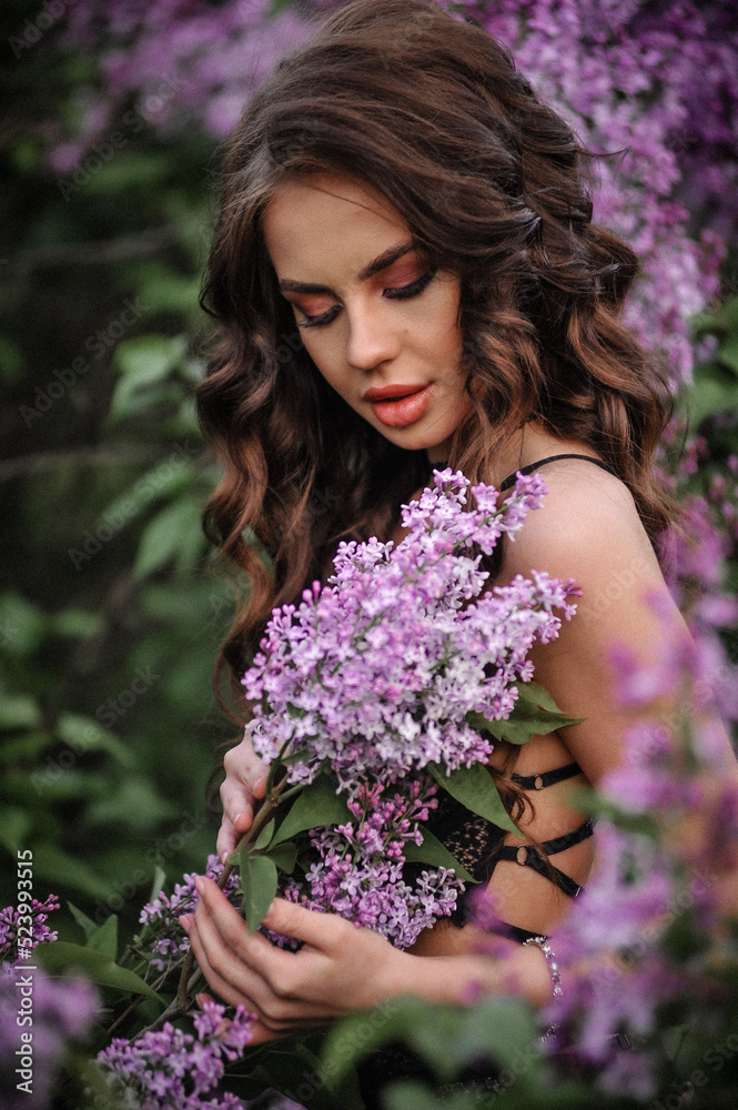 a beautiful girl with makeup and hair styling in underwear stands in a garden with lilacs on a summer evening a beautiful girl with makeup and hair styling in underwear stands in a garden with lilacs on a summer evening