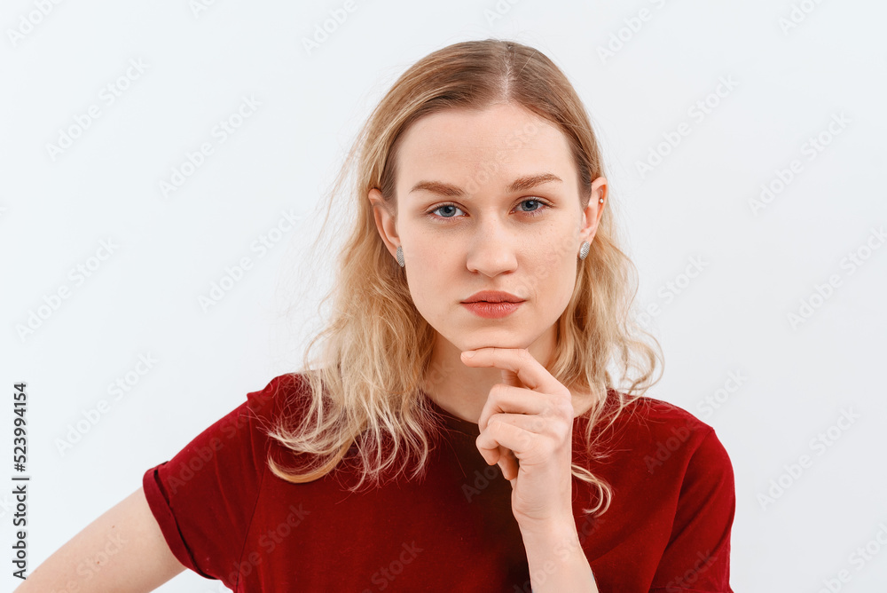 Young emotional woman. Close up portrait of serious blonde girl 20s, looking at camera with angry expression, wears casual red tshirt. Indoor studio shot on white background. Facial expression concept Young emotional woman. Close up portrait of serious blonde girl 20s, looking at camera with angry expression, wears casual red tshirt. Indoor studio shot on white background. Facial expression concept
