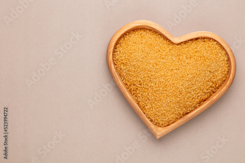 Brown sugar in heart wooden bowl shape on pasttel background.