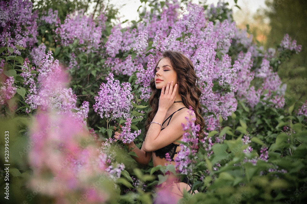 a beautiful girl with makeup and hair styling in underwear stands in a garden with lilacs on a summer evening a beautiful girl with makeup and hair styling in underwear stands in a garden with lilacs on a summer evening